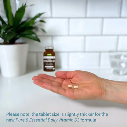 Hand holding two tablets with a bottle of Vitamin D3 in the background on a white surface.